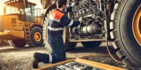 DALL·E 2024-10-22 01.11.43 - A detailed image of a mechanic performing maintenance on heavy machinery in a construction site. The machinery is large and industrial, with visible t